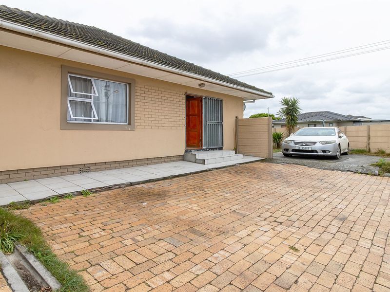 Front exterior view of a single-story house featuring a paved driveway, tiled entrance area, and perimeter walling.