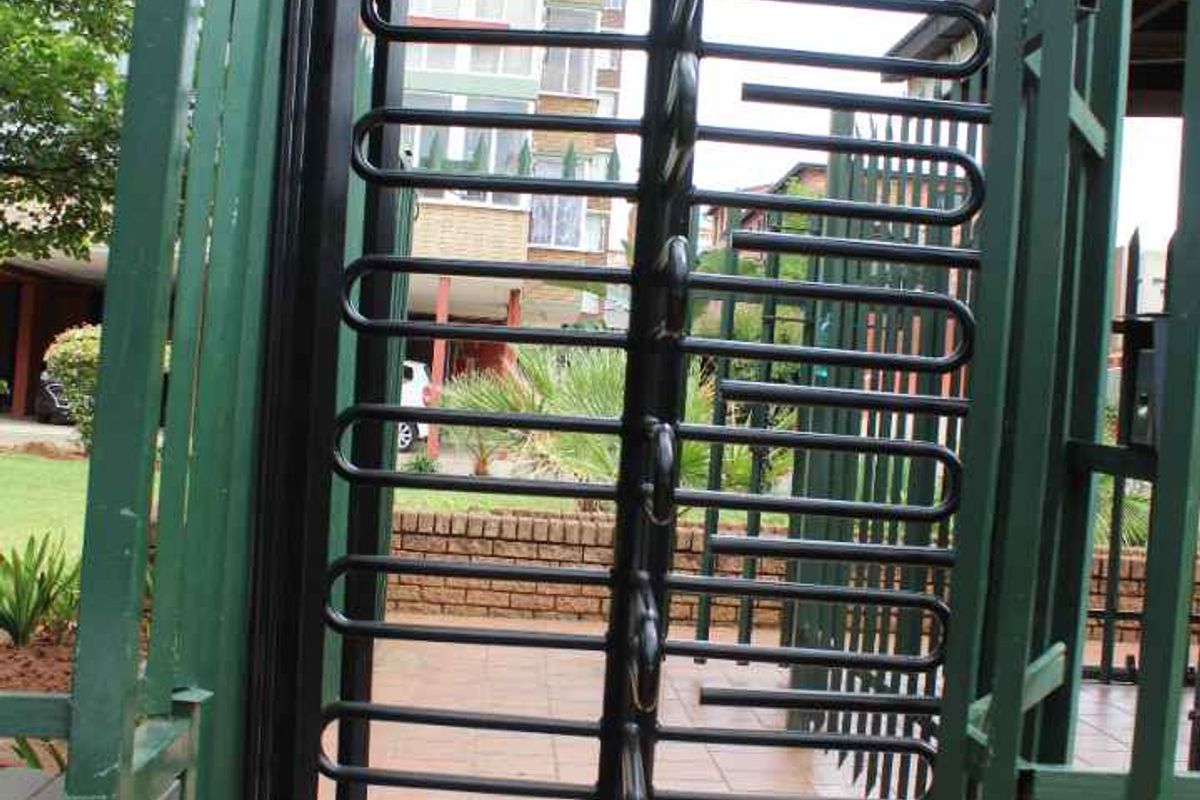 A secure pedestrian entrance featuring a metal turnstile, brick pillars, and perimeter fencing with razor wire for added security.