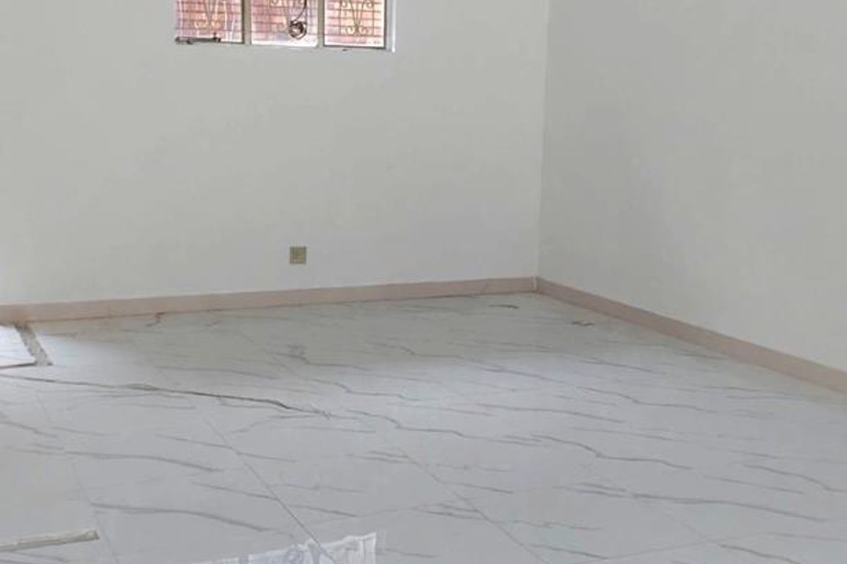 A bright, empty office space featuring modern marble-effect tiled flooring, a window with security bars, and a built-in air conditioning unit.