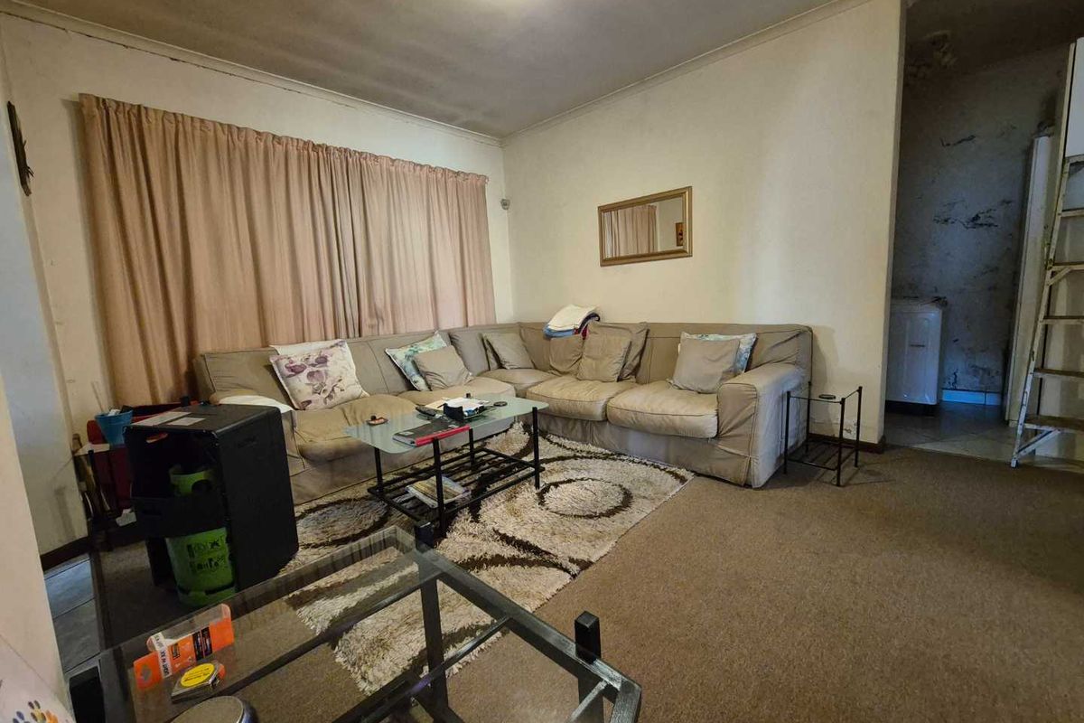 A living room space featuring carpet flooring and coving, currently showing signs of wear and wall surface deterioration requiring maintenance.