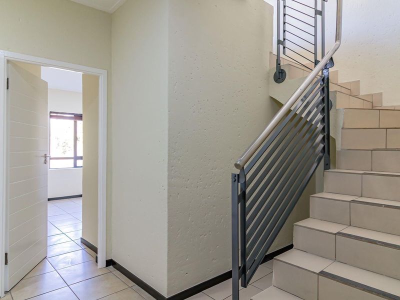 A bright, tiled hallway featuring a staircase with a modern metal balustrade and access to an adjacent room.