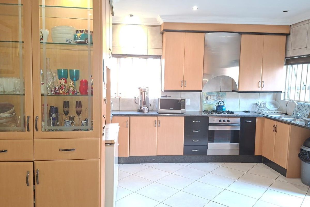 A functional kitchen featuring light wood cabinetry, stainless steel appliances, a built-in oven, hob, extractor fan, and tiled flooring.