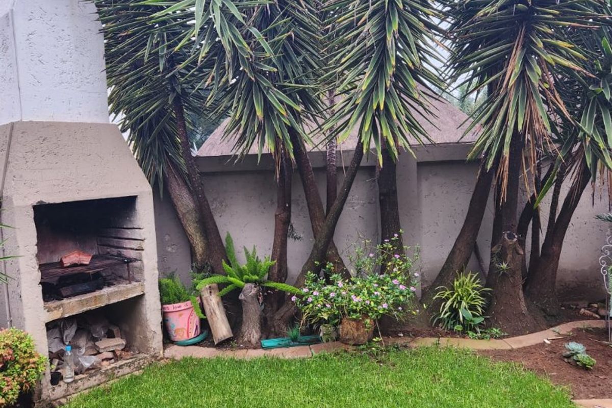 A private rear garden area featuring a built-in masonry braai, established yucca trees, and a well-maintained lawn enclosed by a perimeter wall.