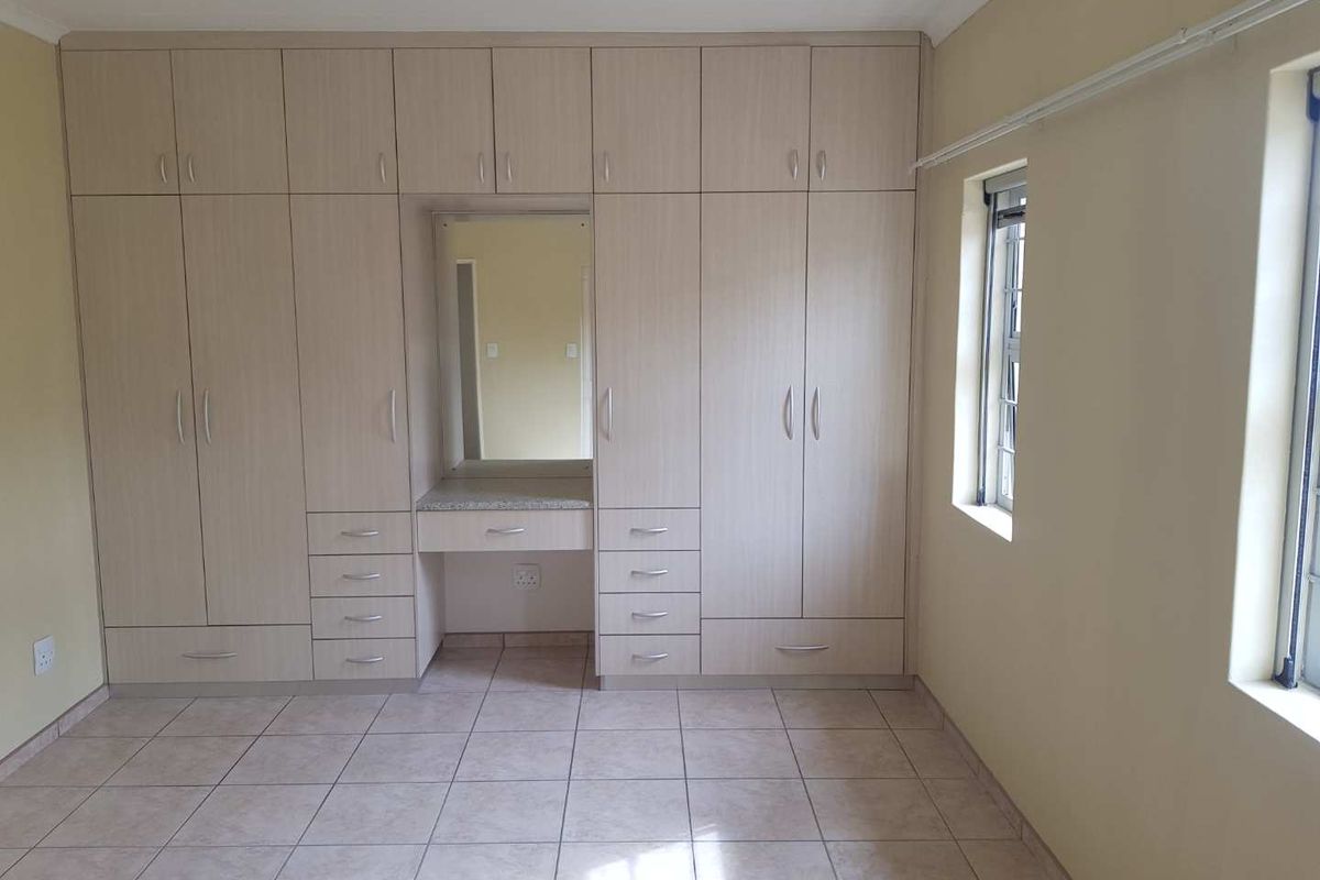 A bedroom featuring extensive built-in cabinetry with a central vanity area, tiled flooring, and large windows providing natural light.