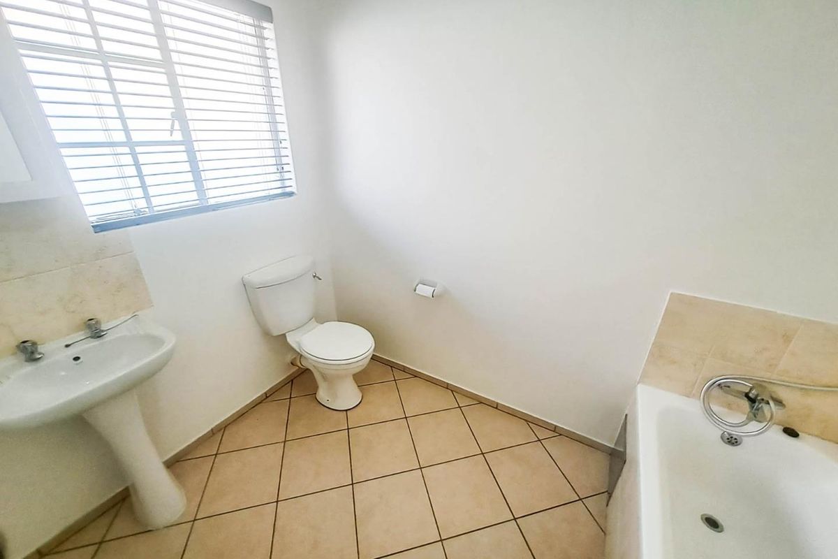 A functional bathroom featuring a pedestal basin, toilet, and bathtub with neutral floor tiling and window blinds.