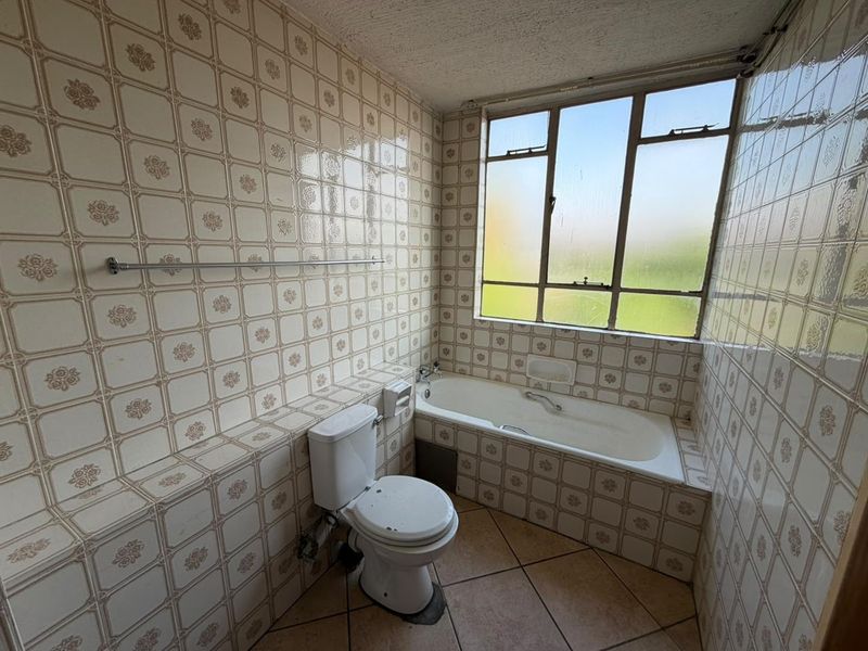 A dated bathroom featuring original wall tiling, a built-in bathtub, and a toilet, requiring modernization to improve its aesthetic and functional appeal.