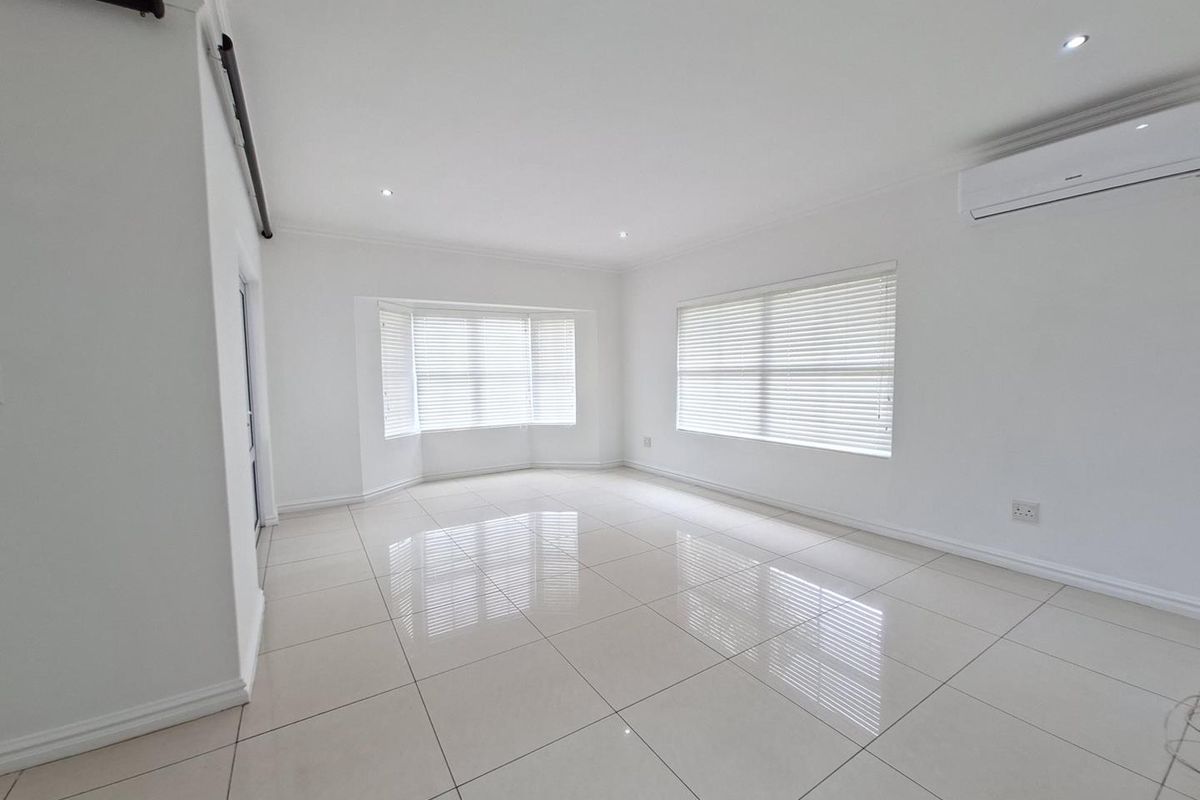 A bright, spacious, and empty living area featuring polished tiled floors, recessed lighting, a split-system air conditioner, and large windows with fitted venetian blinds.