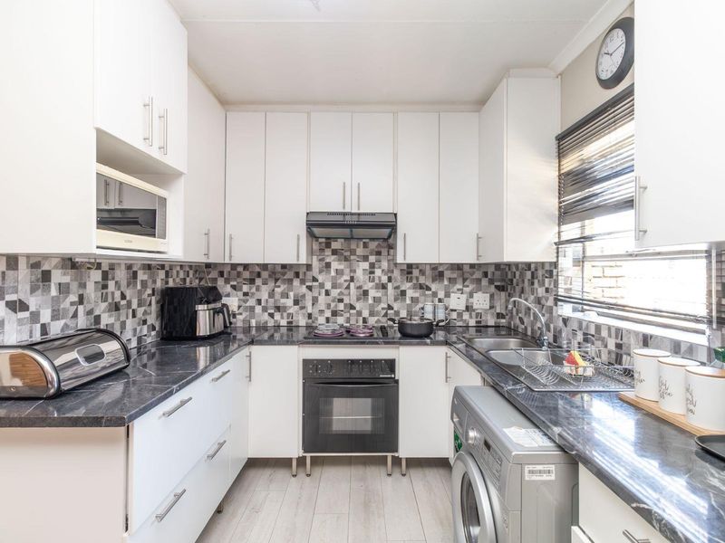 A well-maintained kitchen featuring white cabinetry, dark laminate countertops, a built-in oven with hob, extractor fan, and a tiled mosaic backsplash.