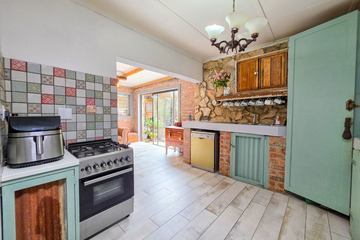 Rustic kitchen featuring a stone accent wall, gas stove, tiled splashback, and light-toned tiled flooring with direct access to an adjacent living area.