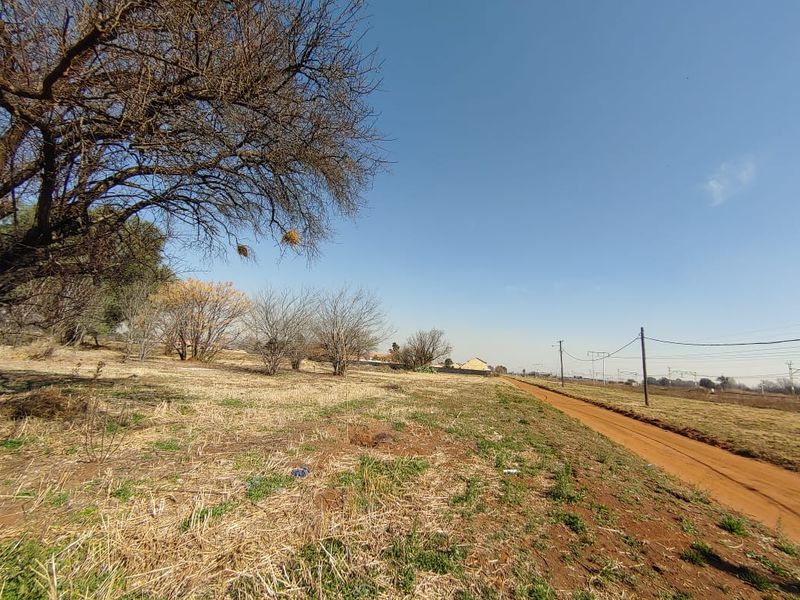 A view of a vacant commercial land plot featuring a dirt road access and existing utility infrastructure.