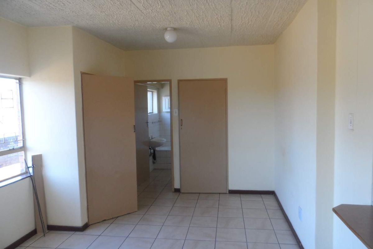 An empty bedroom featuring tiled flooring, textured ceilings, and direct access to an en-suite bathroom area.