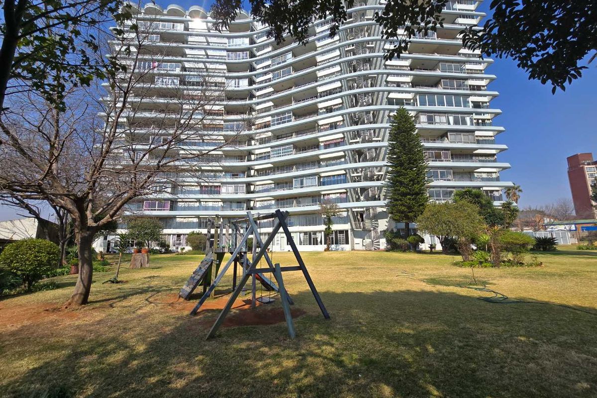 A view of a multi-story apartment building featuring private balconies, set against a well-maintained communal garden and lawn area.
