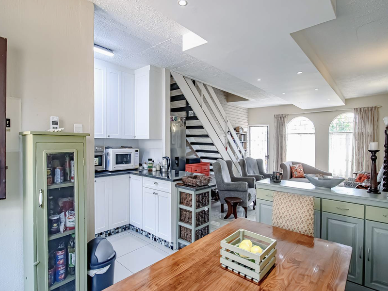 Open-plan living and kitchen area featuring white cabinetry, tiled flooring, a staircase, and arched windows providing natural light.