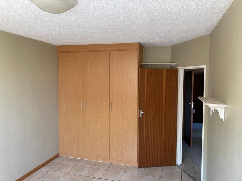 A vacant bedroom featuring built-in wooden cupboards, tiled flooring, and a textured ceiling, offering a neutral canvas for potential updates.