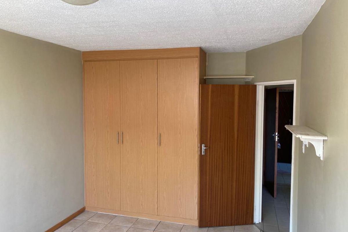 A vacant bedroom featuring built-in wooden cupboards, tiled flooring, and a textured ceiling, offering a neutral canvas for potential updates.