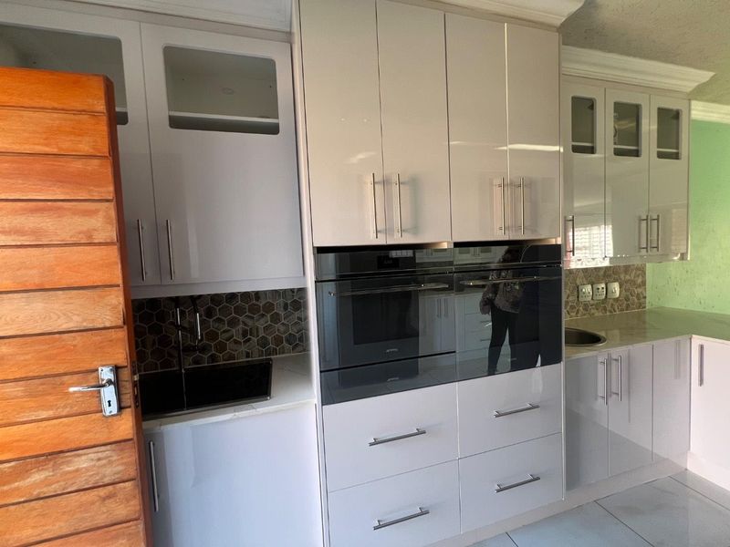 Modern kitchen featuring high-gloss cabinetry, integrated appliances including a built-in oven and microwave, stone countertops, and a stylish hexagonal tiled backsplash.