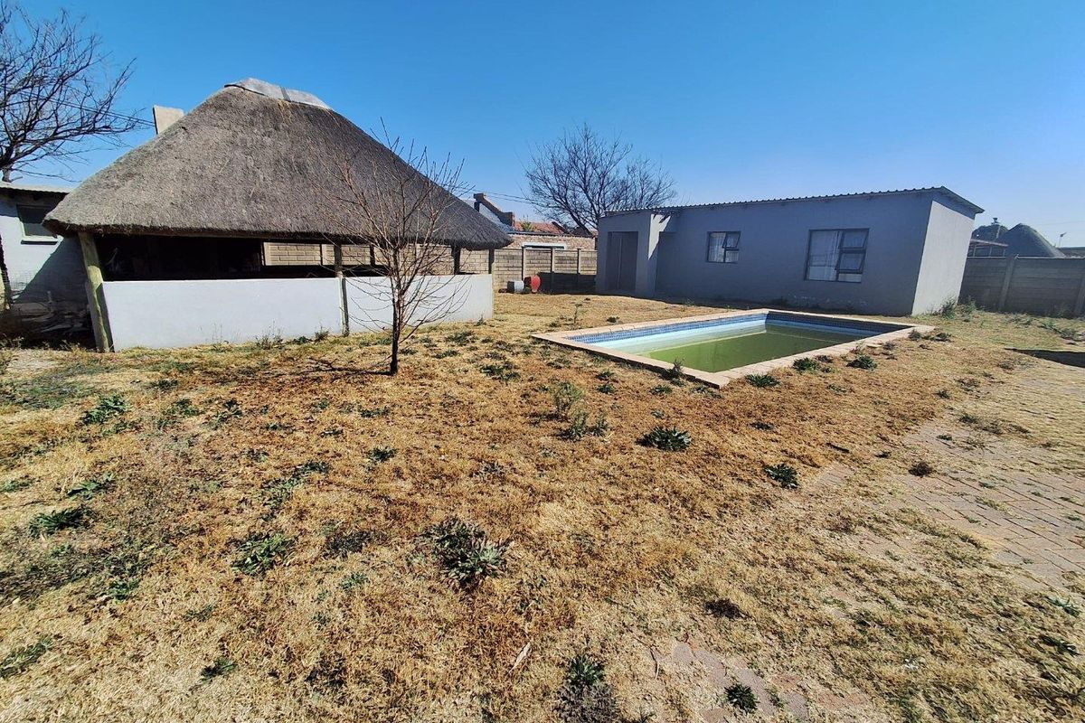 Rear garden area featuring a thatched lapa, a swimming pool, and boundary walling, requiring landscaping and pool maintenance.