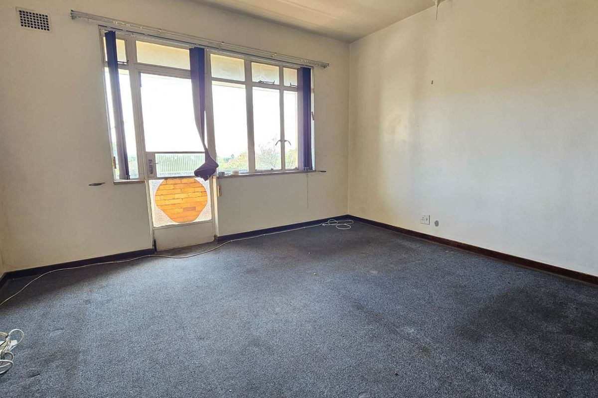 An empty bedroom featuring wall-to-wall carpeting, large windows, and access to a balcony area, offering a blank canvas for renovation.