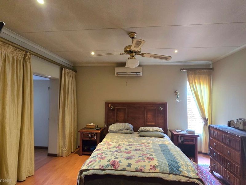 A spacious bedroom featuring laminate flooring, a ceiling fan, and a wall-mounted split-system air conditioner for climate control.