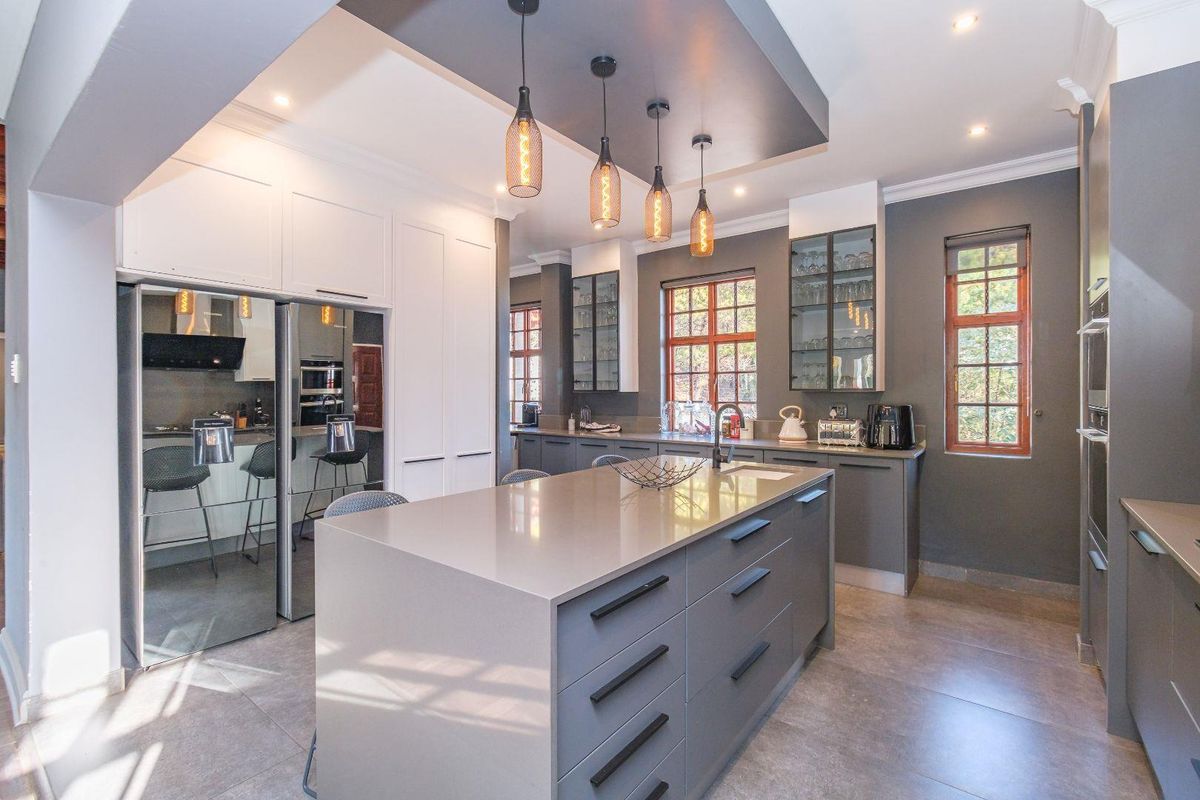 Modern kitchen featuring a large central island with quartz countertops, sleek grey cabinetry, glass-front display units, and stylish pendant lighting.