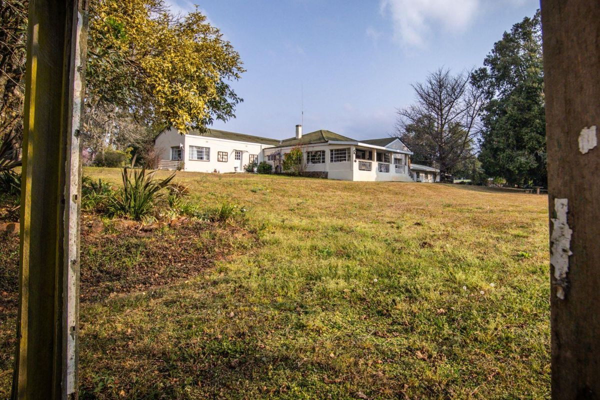 A view of the rear elevation of the farmhouse, featuring a covered patio area and expansive surrounding lawn and mature trees.