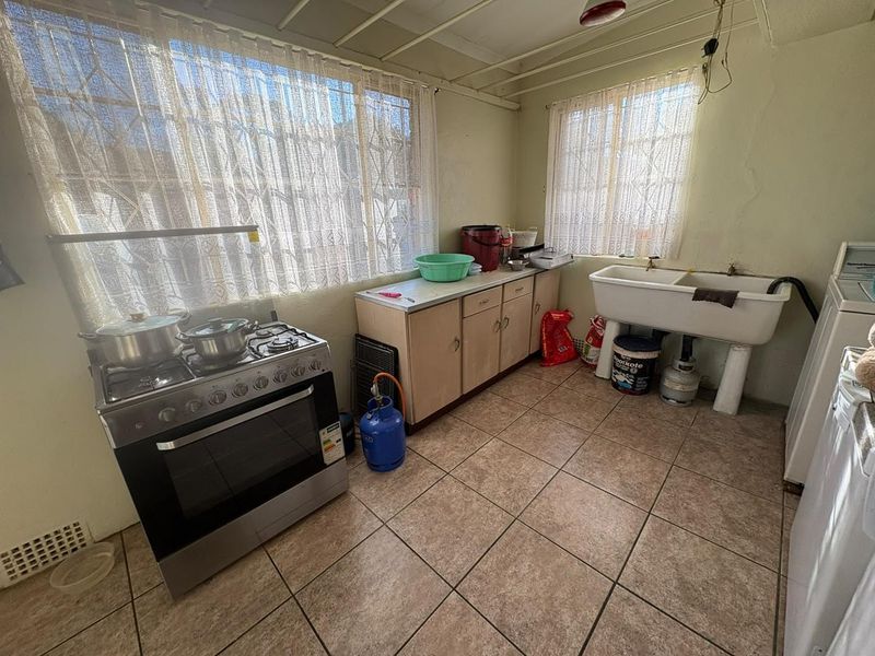 A functional kitchen area featuring tiled flooring, built-in cabinetry, a gas stove, and a double basin utility sink, requiring cosmetic updates.