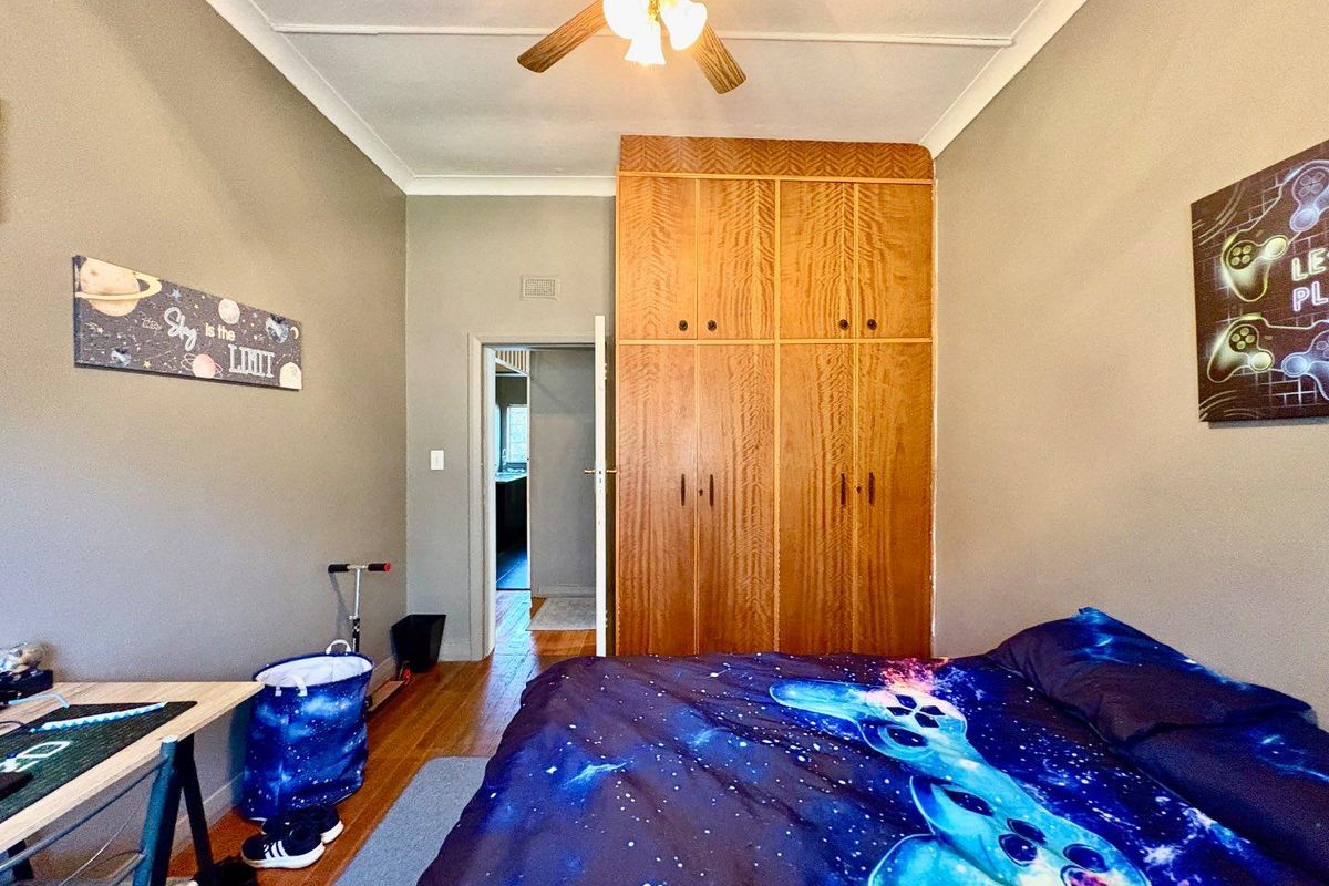A bedroom featuring built-in wooden wardrobes, timber flooring, and a ceiling fan, providing a functional space with classic storage solutions.