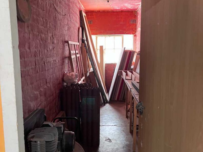 A narrow utility or storage space featuring exposed brick walls and concrete flooring, currently used for industrial equipment storage.