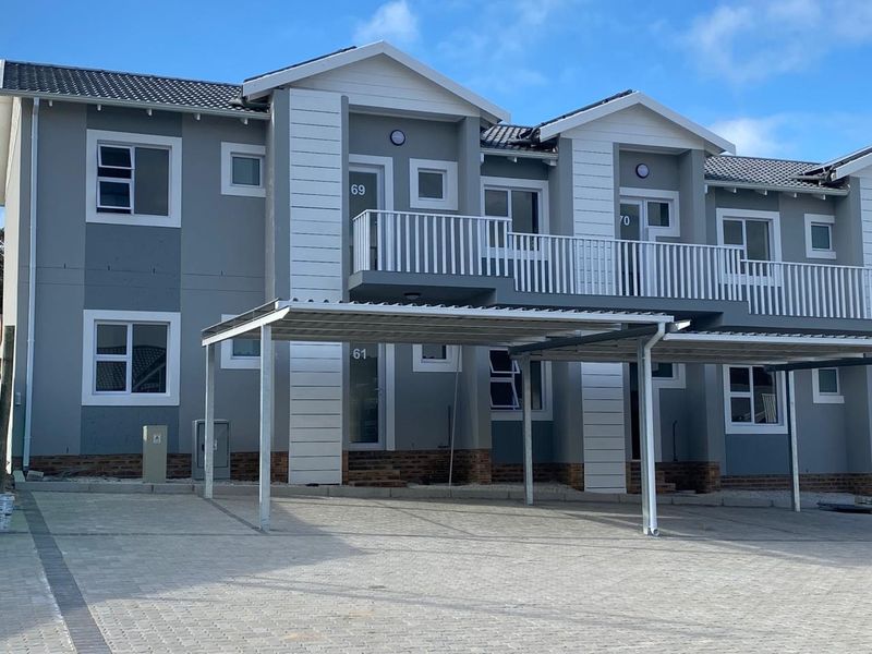 Modern apartment complex exterior featuring grey facade, white trim, private balconies, and dedicated covered carport parking spaces.