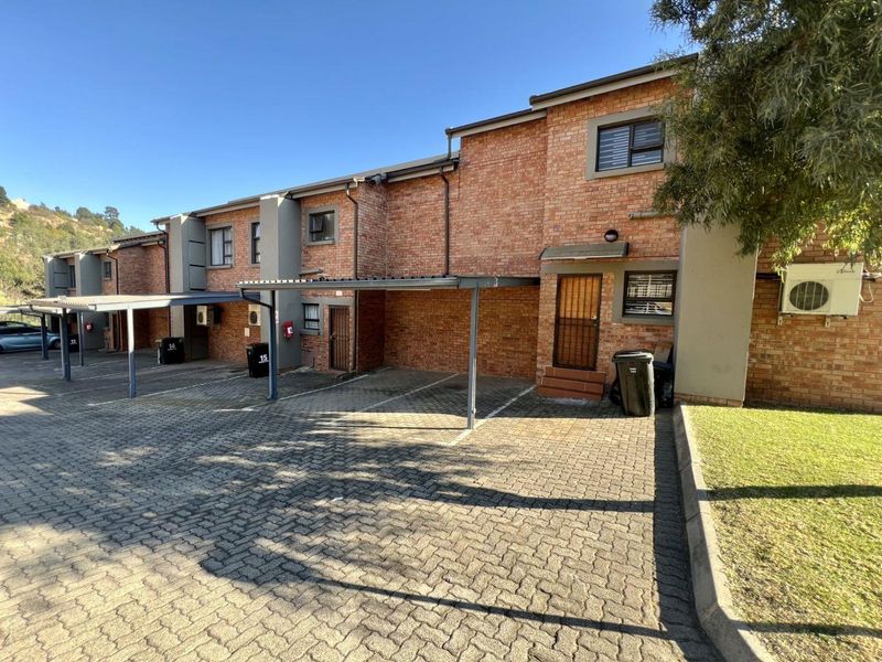 Front exterior view of a brick townhouse complex featuring covered parking bays, paved driveway, and security gates.