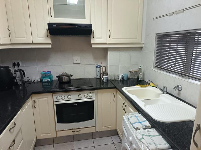A functional kitchen featuring cream cabinetry, dark granite countertops, a built-in oven with hob, and a double basin sink with tiled splashbacks.