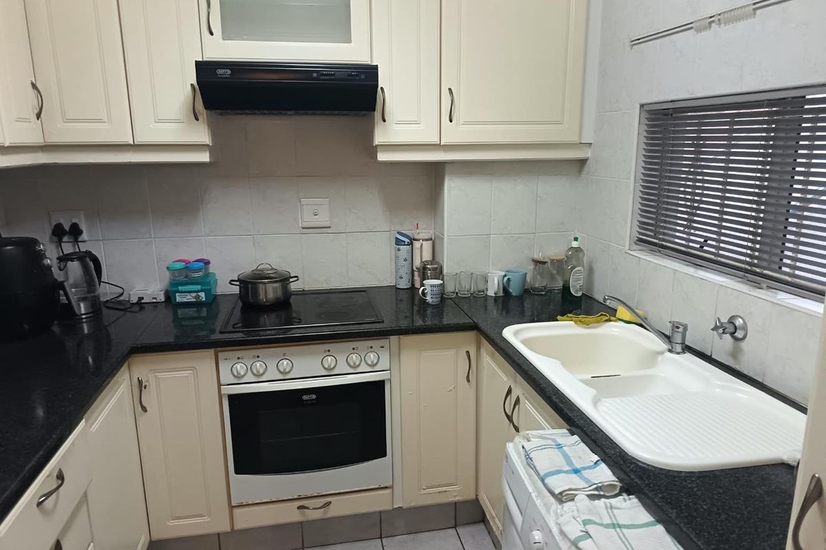 A functional kitchen featuring cream cabinetry, dark granite countertops, a built-in oven with hob, and a double basin sink with tiled splashbacks.