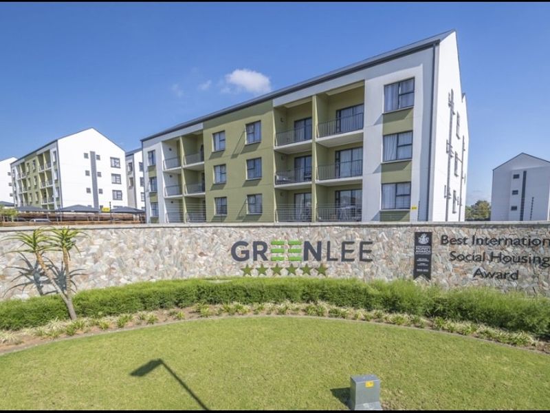 A well-maintained multi-story apartment complex featuring modern architecture, private balconies, and a landscaped entrance with stone feature wall.