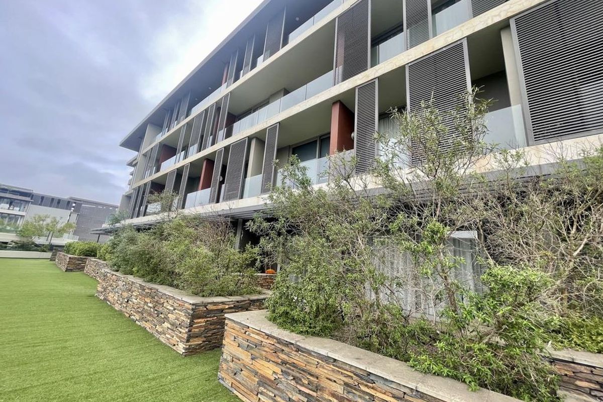 Modern apartment building exterior featuring stacked stone retaining walls, landscaped garden beds, and private balconies with integrated privacy screens.