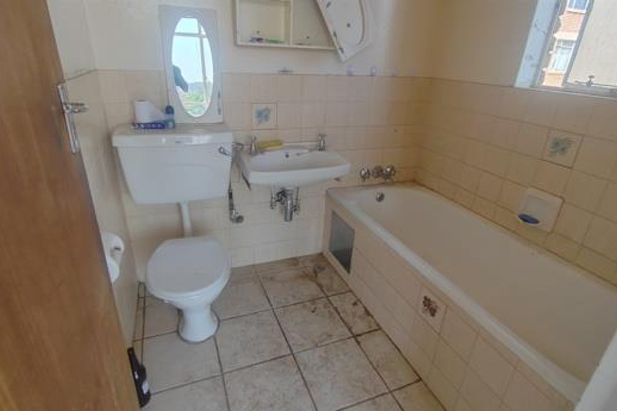 A dated bathroom featuring a standard bathtub, wall-mounted basin, and toilet with original ceramic wall tiling and floor tiles.