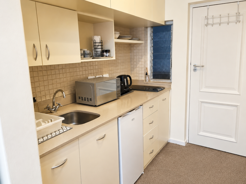 Compact kitchen featuring built-in cabinetry, laminate countertops, a stainless steel sink, tiled splashback, and a built-in hob.