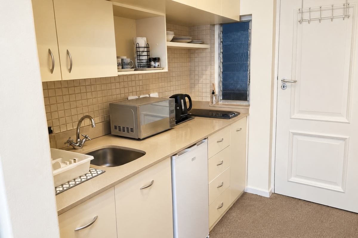 Compact kitchen featuring built-in cabinetry, laminate countertops, a stainless steel sink, tiled splashback, and a built-in hob.