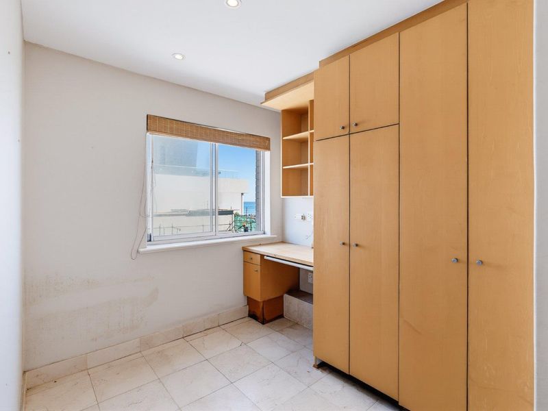 A bedroom featuring built-in wooden cupboards, a matching integrated desk, tiled flooring, and a window with views.