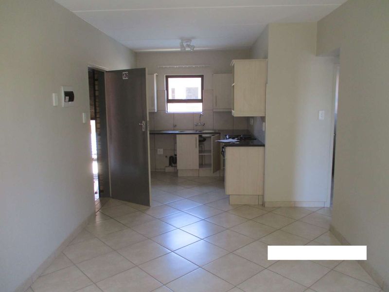 Open-plan living area featuring tiled flooring and a functional kitchen with built-in cabinetry, hob, and extractor fan.