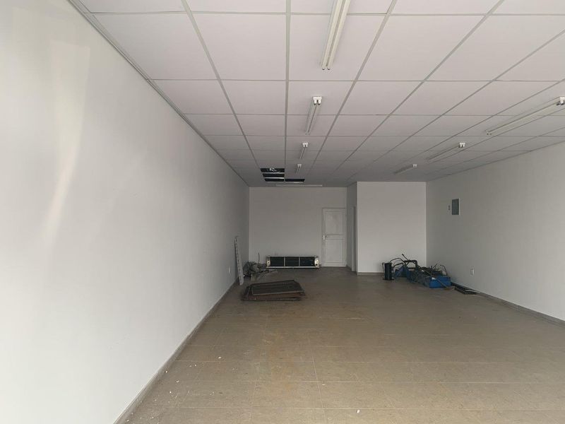 An empty open-plan retail space featuring tiled flooring and a suspended ceiling with some missing panels, suitable for various commercial uses.