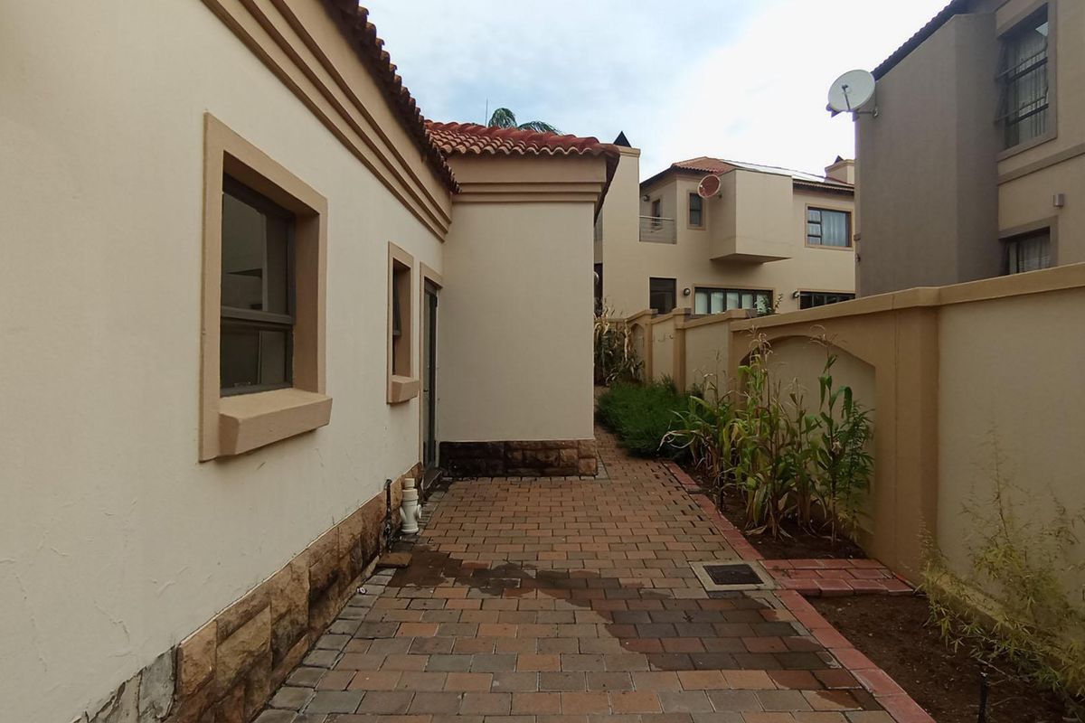 A side exterior view of the property featuring brick paving, perimeter walling, and access to the rear garden area.