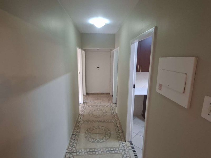 A clean, functional hallway featuring patterned tiled flooring, providing access to adjacent rooms and equipped with a wall-mounted electrical distribution board.