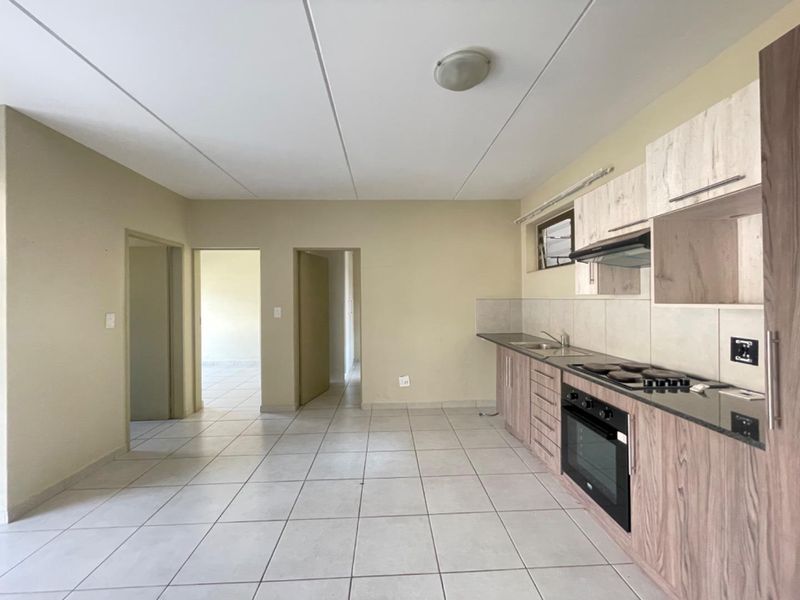 An open-plan kitchen area featuring wood-look cabinetry, built-in appliances, and neutral tiled flooring, offering a clean and functional space.