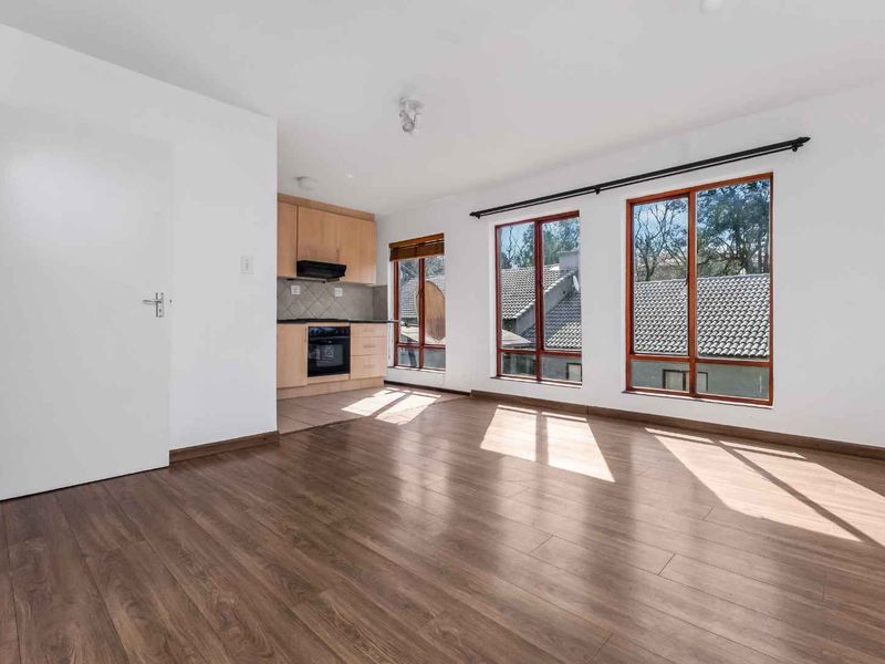Bright open-plan living area featuring laminate flooring and a compact kitchen with built-in cabinetry, oven, and extractor fan.