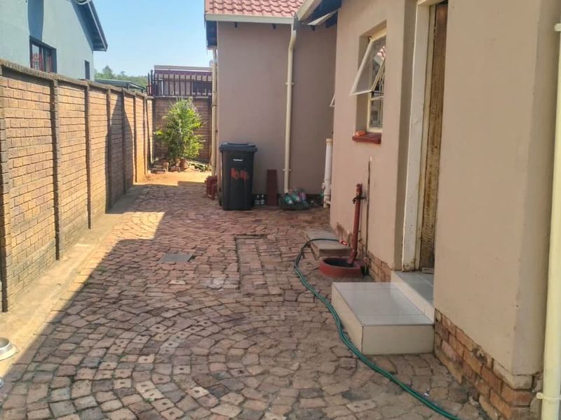 A side exterior view of the property featuring brick paving, a boundary wall, and a tiled entrance step leading to the side of the house.