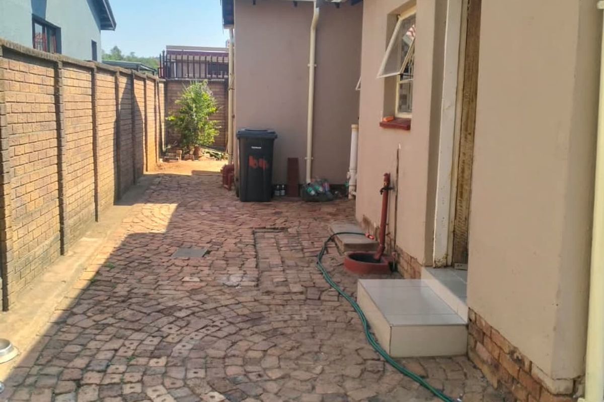 A side exterior view of the property featuring brick paving, a boundary wall, and a tiled entrance step leading to the side of the house.