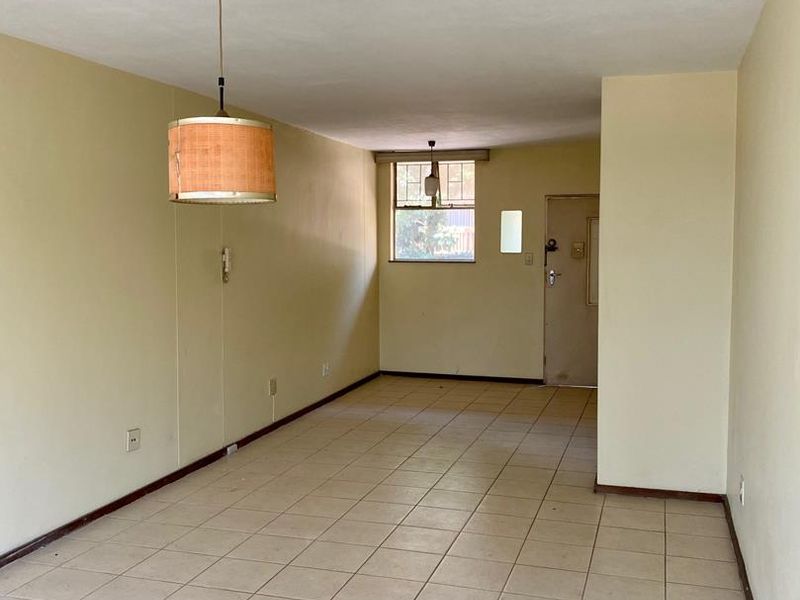 An empty, open-plan living area featuring neutral ceramic floor tiles, simple pendant lighting, and a functional layout ready for renovation or staging.