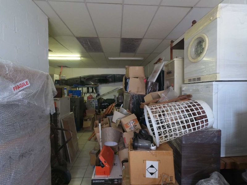 A cluttered utility or storage space featuring a suspended ceiling, fluorescent lighting, and tiled flooring, currently used for general storage.
