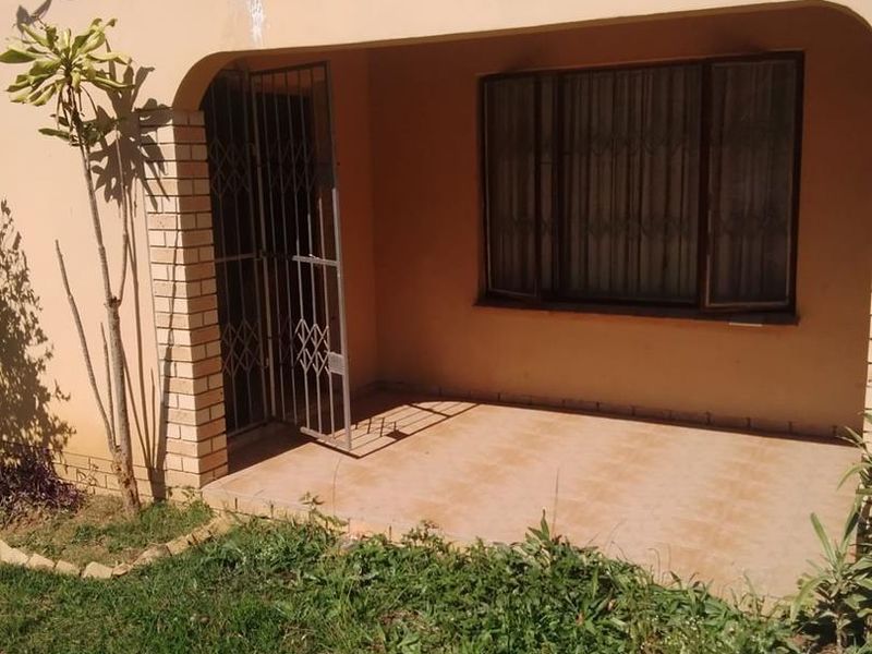 A covered patio area featuring tiled flooring, a security gate, and a window with security bars, providing a functional outdoor space.