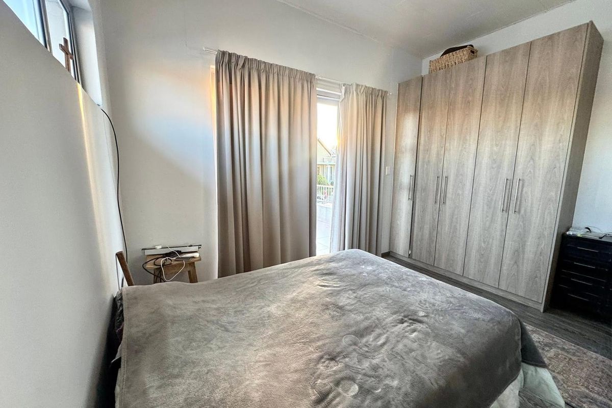A well-lit bedroom featuring built-in wooden wardrobes, laminate flooring, and direct access to an outdoor area through a sliding glass door.
